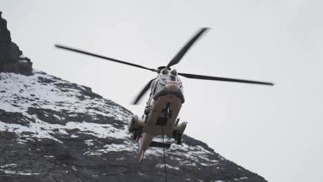 cargo helicopter with lifting cable and load attached landing in the difficult-to-reach mountainous terrain