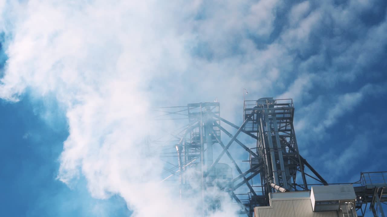 Smoke from the chimney of the grain dryer at the elevator. Metal structures against the blue sky. Pollution the environment
