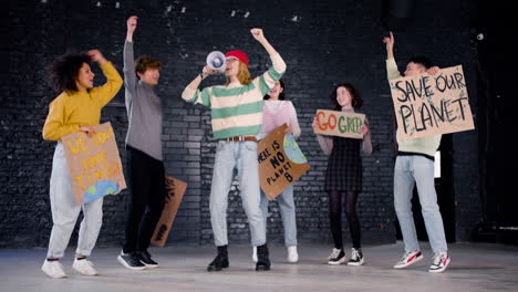 happy young environmental activists with placards and megaphone jumping and  hugging while protesting against climate change inaction