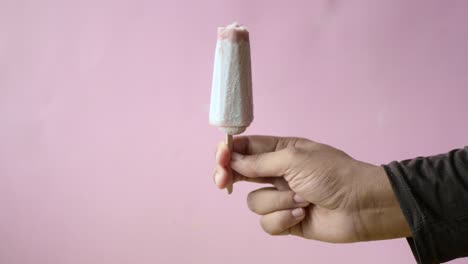 hand holding a popsicle on a pink background