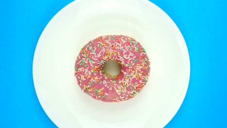 girar las rosquillas cubiertas de glaseado rosa con salpicaduras en un plato blanco sobre un fondo azul.
