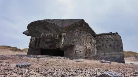 a large, dilapidated section of a ww2 bunker with a gun porthole stands on the beach. europe denmark