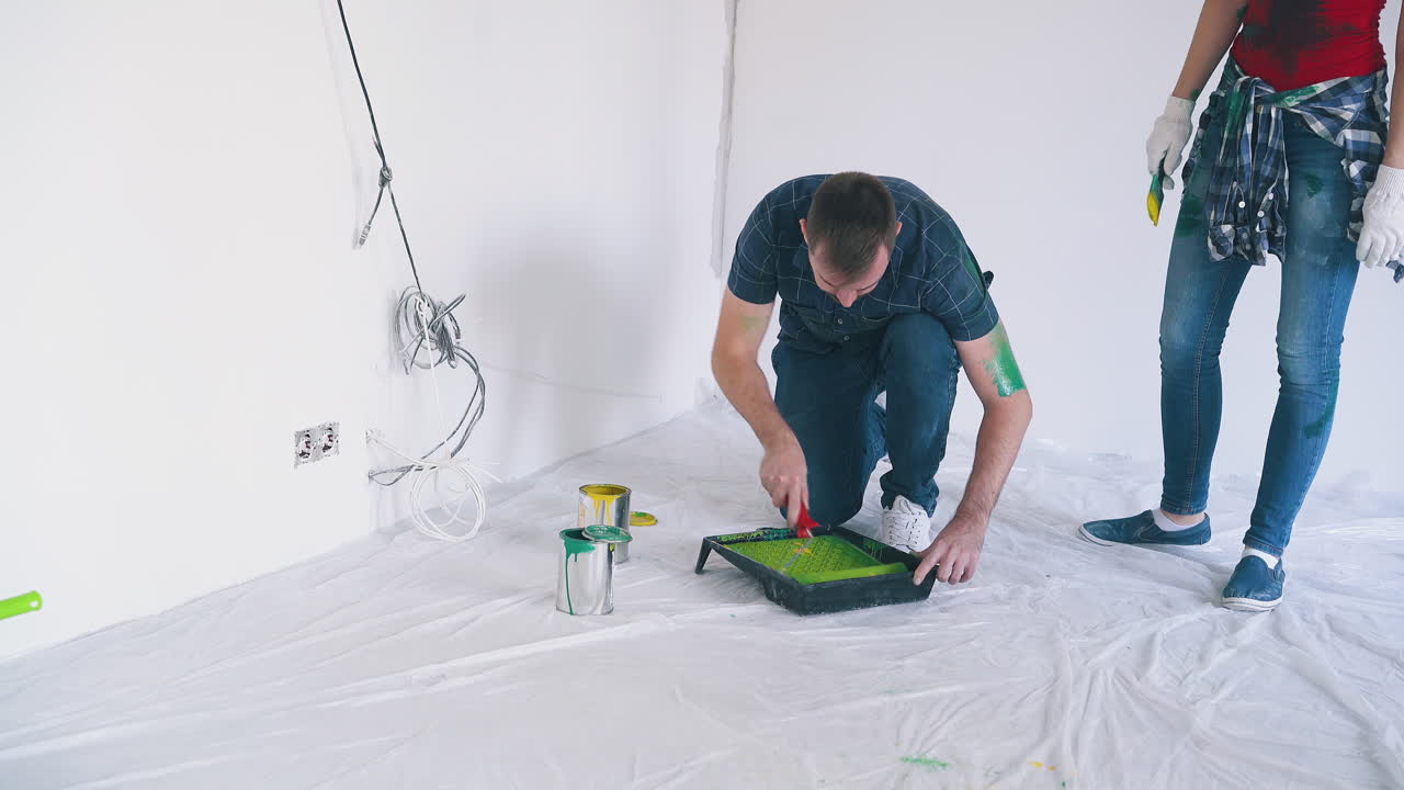 hombre mezcla sombras de pintura cerca de su esposa probando el color en la habitación