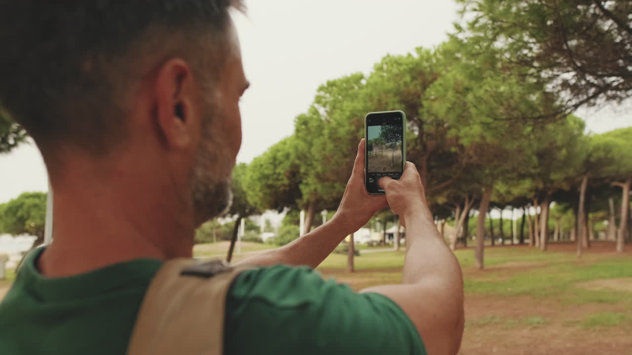 Homem fotografando árvore com celular no parque
