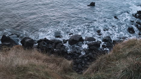 Top-down-view-looking-over-cliff-of-Hellisandur,-Iceland,-ocean-surf-on-rocks