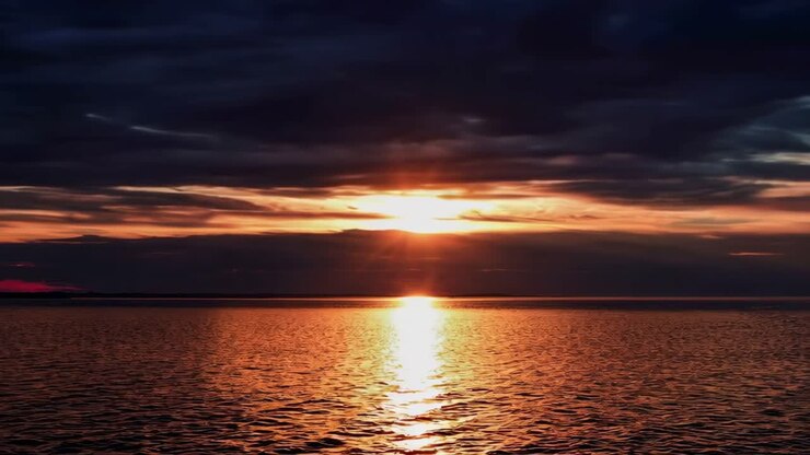 Ein ruhiger Sonnenuntergang über dem Meer mit dramatischen Wolken, aus einem niedrigen Winkel aufgenommen