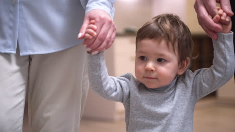 parents holding their baby's hands, helping him take his first steps at home