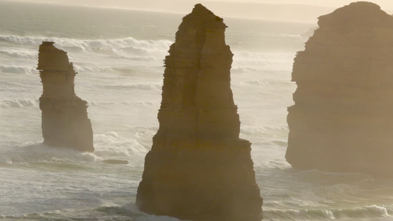 En fredfyldt udsigt over klippeformationerne De Tolv Apostle langs Great Ocean Road, fanget i blødt, gyldent solnedgangslys.