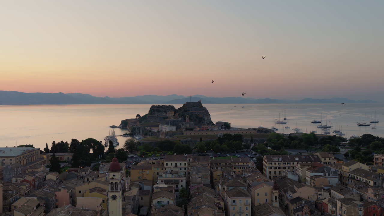 Panoramic drone video of Corfu old town and the old fortress at dawn, with vibrant pre-sunrise colors and swallows flying in the sky