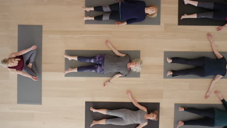 yoga class instructor teaching mature women group meditation practicing corpse pose enjoying mindfulness exercise in studio