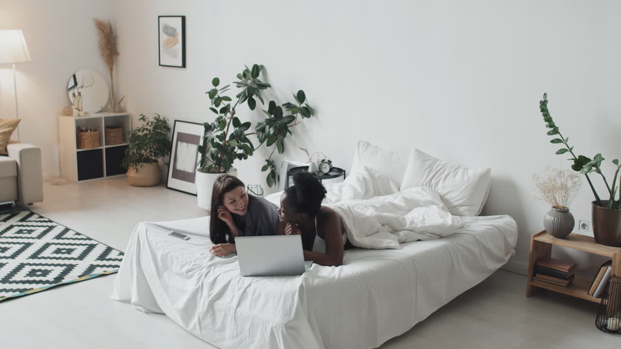 Laughing Lesbian Couple with Laptop Relaxing on Bed