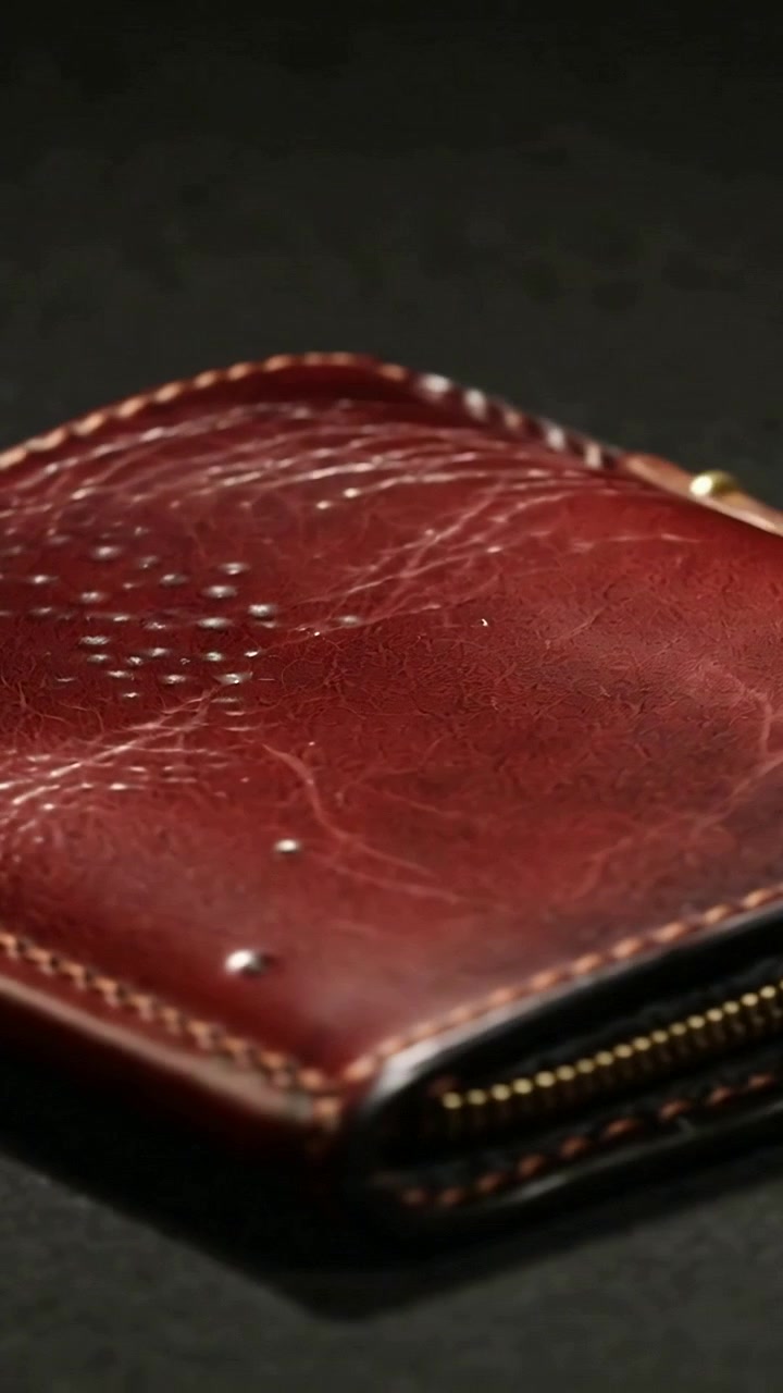 Video verticale: Panoramica che mostra una pochette in pelle bordeaux su un tappetino, esponendo i denti della cerniera per l'usura.
