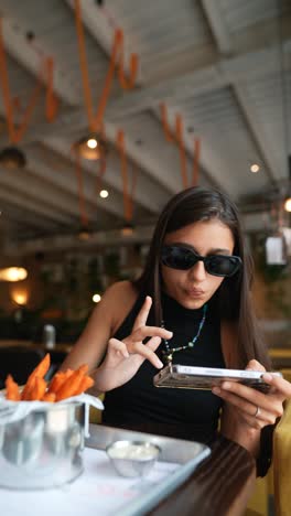 woman using phone while eating sweet potato fries in a cafe