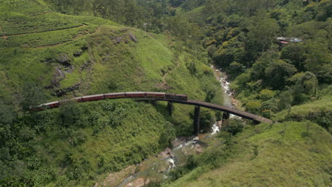 establishing aerial drone shot of diesel passenger train crossing demodara iron bridge on sunny day in sri lanka