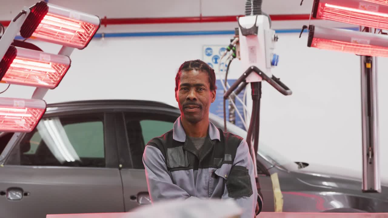 mecánico de automóviles afroamericano cruzando los brazos y mirando a la cámara