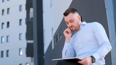 handsome bearded cfo chatting online on ipod outdoors in sunlight against glass building background