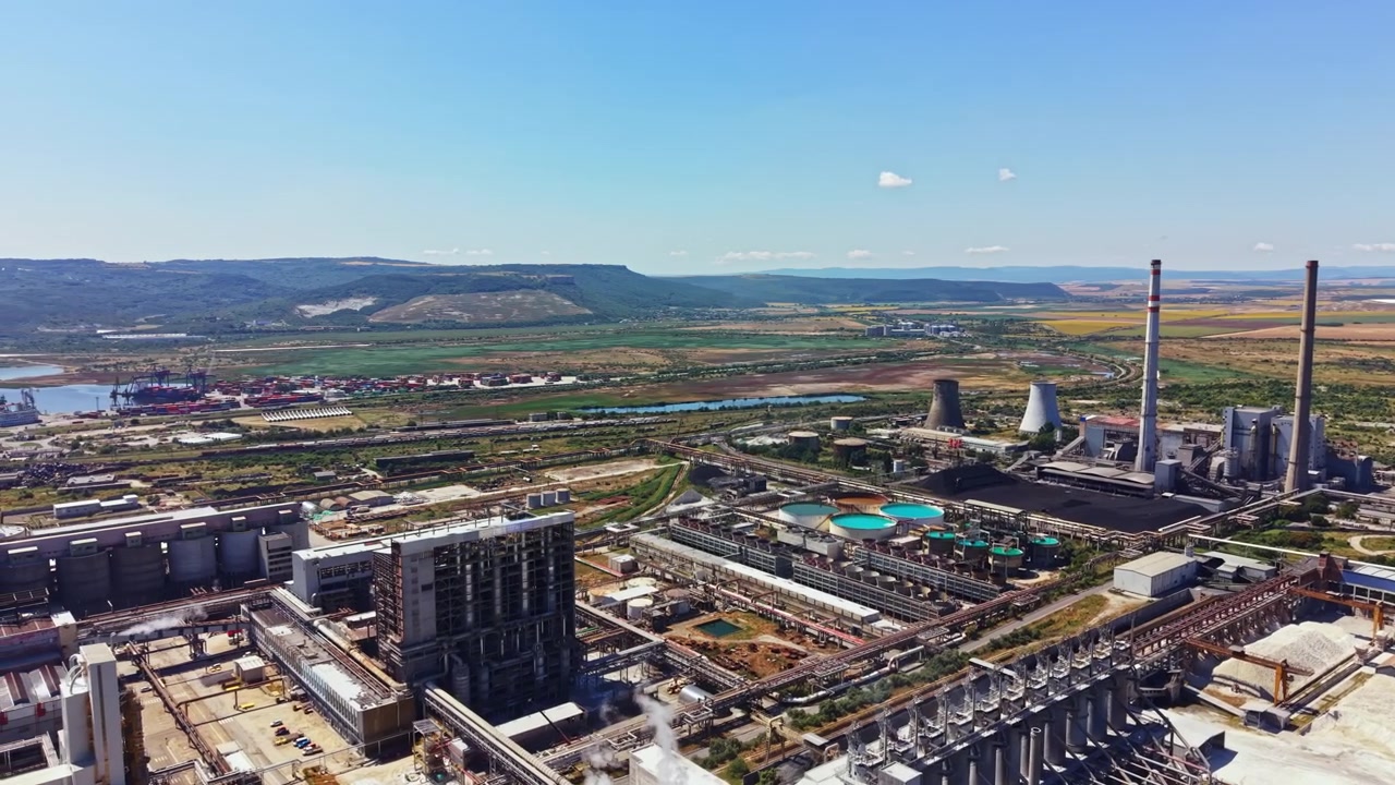 Industrial facility located near a river with towers and machinery involved in production and energy generation in a rural area during the day