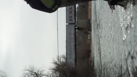 vertical format: narrow focus man walks into frame, fly fishing river