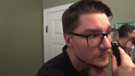 caucasian man with glasses grooming his beard with cordless trimmer