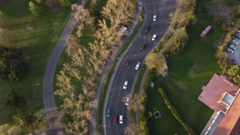 aerial top down of many cars driving on curvy road beside rural park area in buenos aires during sunset time