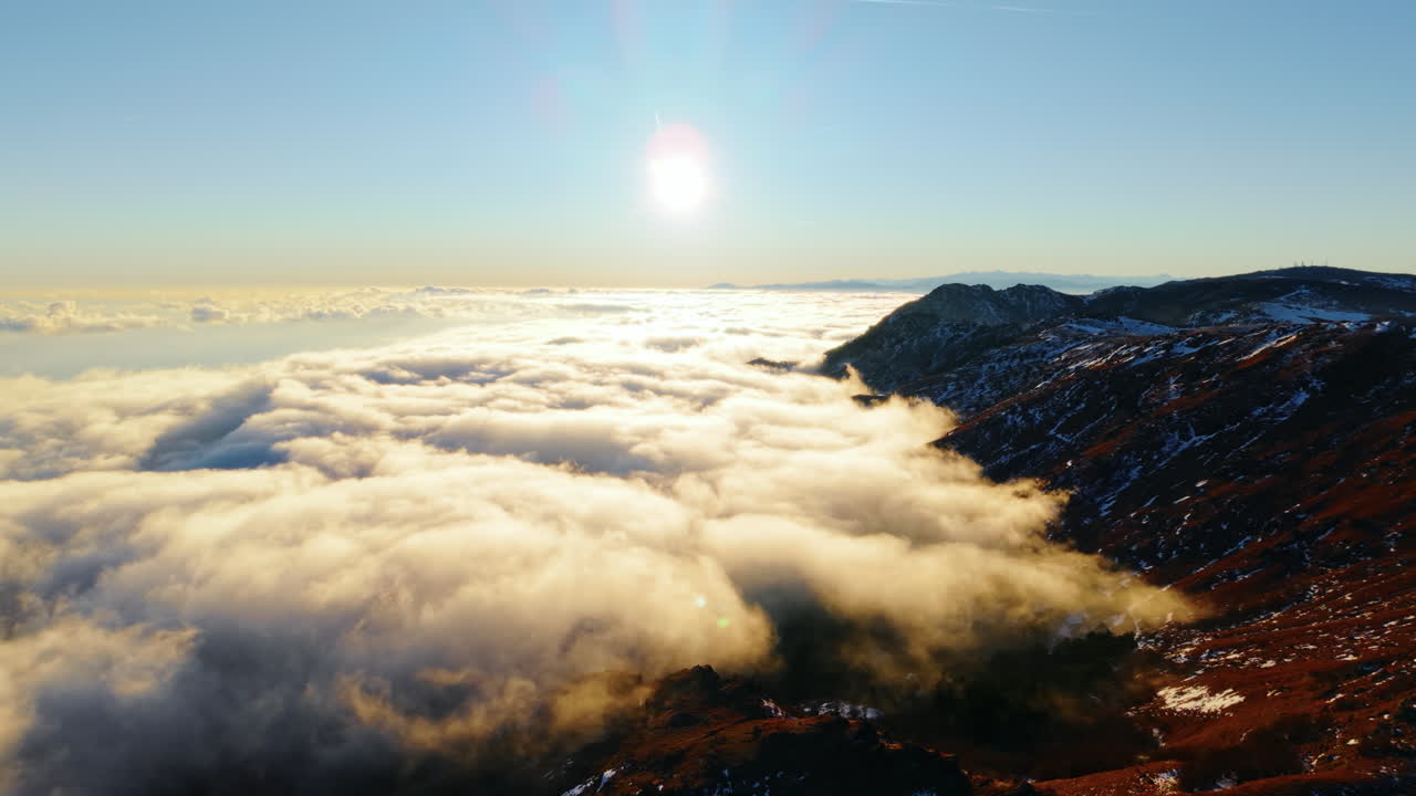 Ripresa aerea all'alba sopra montagne e nuvole, con sole splendente in lontananza