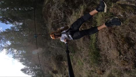 vertical action camera shot of a young man gliding down in high speed on a zipline in canada with beautiful lush green forest around him