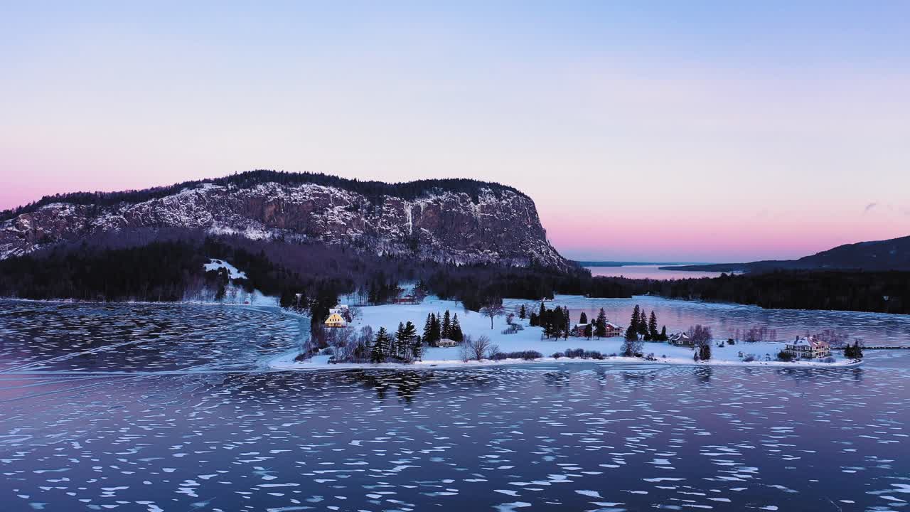 orbitando alrededor de una península en un lago congelado en la base del acantilado de una montaña aislada al amanecer con patrones de líneas y círculos en el hielo