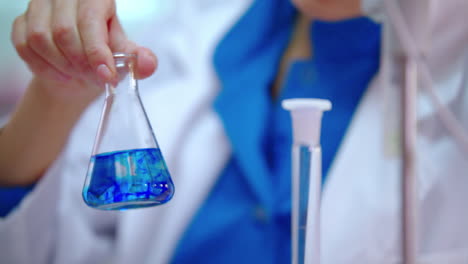 Science-laboratory-research.-Female-scientist-hands-mixing-blue-liquid-in-flask