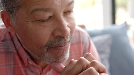 Contemplative-senior-biracial-man-sitting-thinking-in-sunny-living-room-at-home,-slow-motion