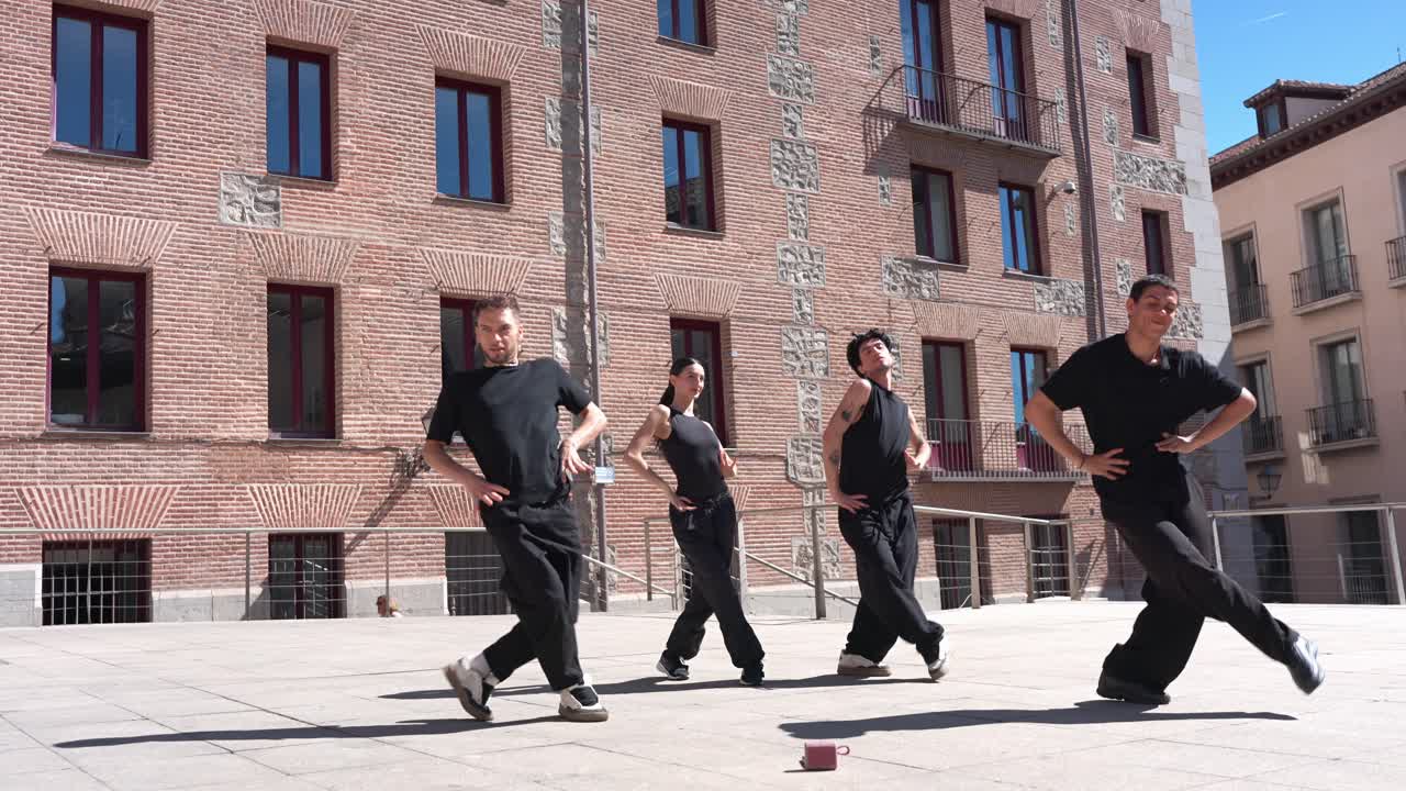 Gruppo energico di giovani ballerini che eseguono una coreografia hip hop in una piazza urbana.