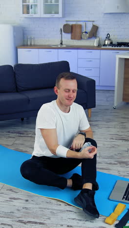 young man exercising at home. man is sitting on a mat on floor and holding balance with a bottle. fitness at home during quarantine. vertical video