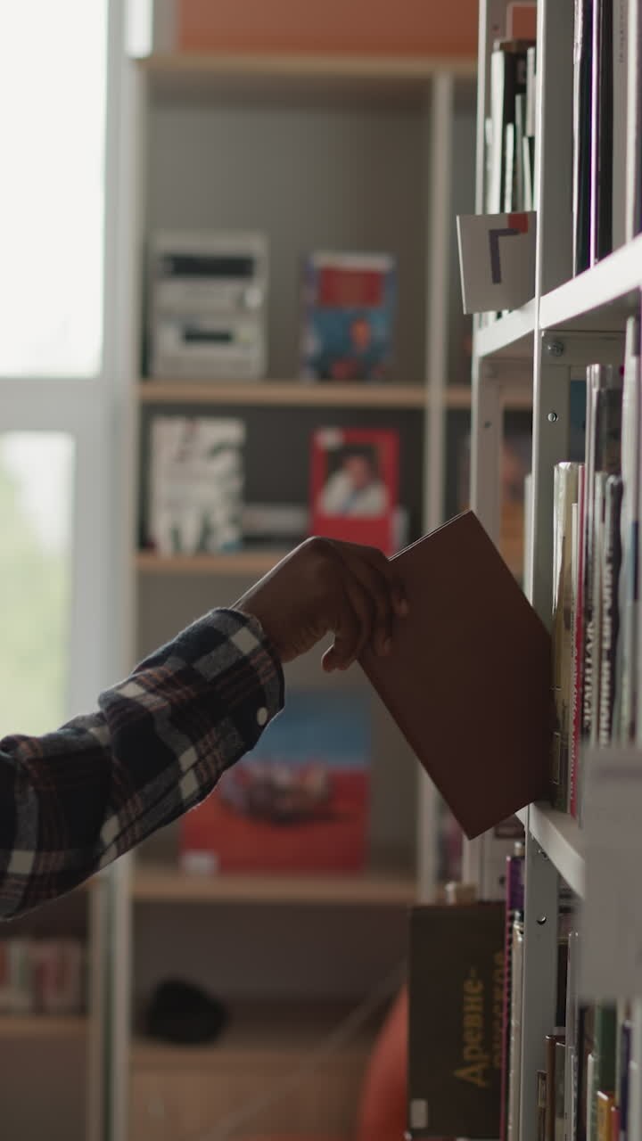 Man picks up book from shelf in library. Dark-skinned male student found right book on shelf and goes to read it. Black guy at state library