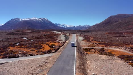 following a vehicle driving on an empty road with snowy mountains in the background