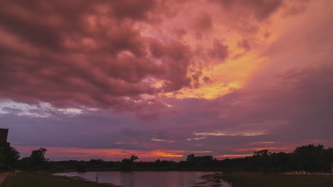 purple pink and red tinted storm clouds spread above pond, time lapse