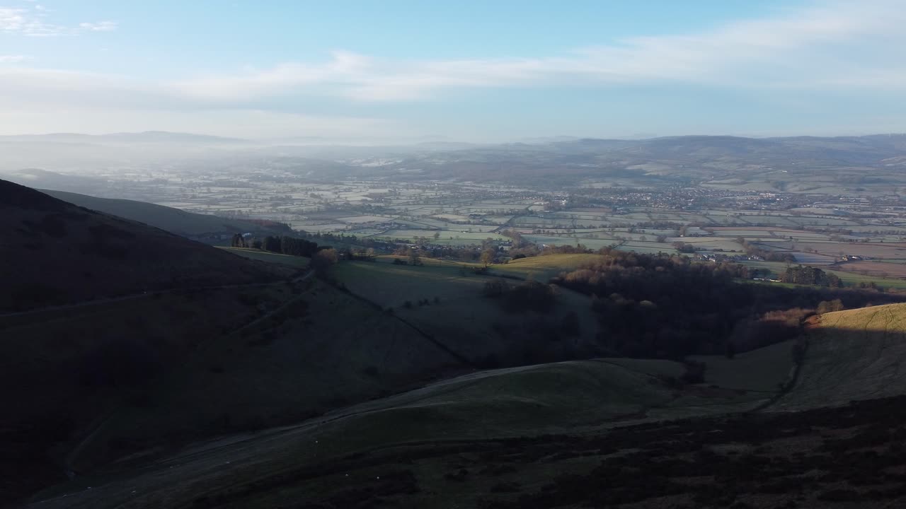 Lontani strati nebbiosi di una panoramica valle montana rurale al sorgere del sole, vista aerea in orbita bassa a destra