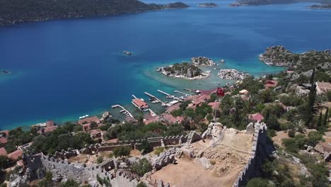 Impresionante-Vista-Aérea-Sobre-Ruinas-Y-Casas-En-La-Costa-Con-Agua-Turquesa-En-La-Antigua-Ciudad-De-Aperlai,-Turquía