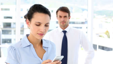 businesswoman texting on her smartphone with colleague behind her