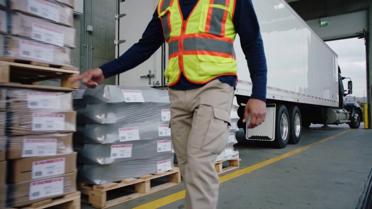 Walking dock worker in hi-vis vest along yellow line after trailer backing, heading to load pallets