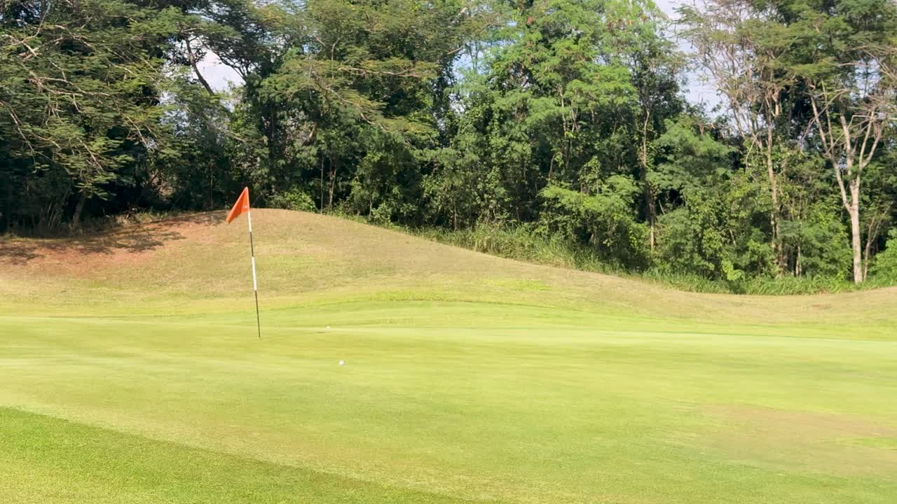 Un golfista tira una pallina attraverso un fairway verde e rigoglioso verso una bandiera arancione distante