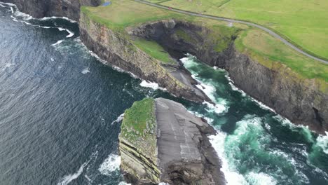 cliffs by the sea with waves crashing, green fields and a road in the distance