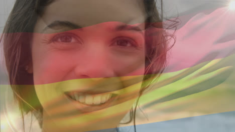 Vídeo-Compuesto-De-Ondear-La-Bandera-De-Alemania-Sobre-El-Retrato-De-Una-Mujer-Caucásica-Sonriendo-En-La-Playa