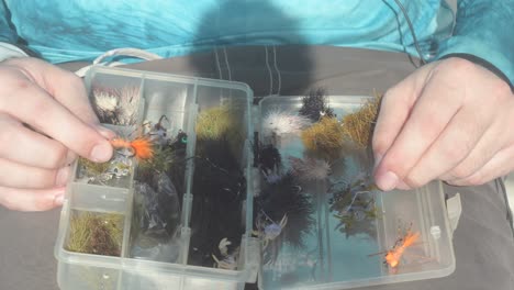 fisherman selects and showcases multicolored flies from plastic saltwater tackle box held on lap