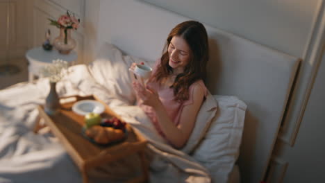 happy female scrolling mobile phone in morning. smiling serene girl holding cup