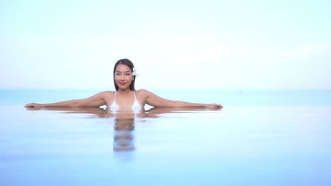 asian fit thai woman with flower in her hair relaxing inside infinity pool front view daytime, hawaii template copy space
