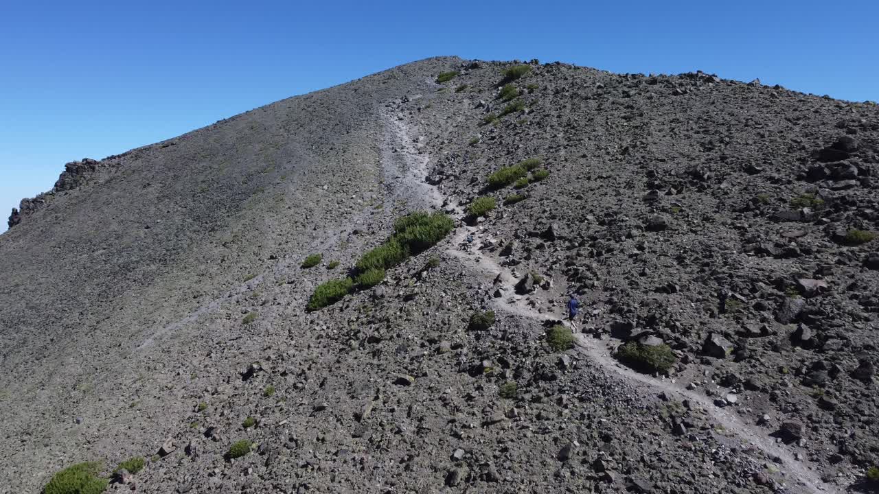 excursionista caminando por un sendero hacia la cima de una montaña rocosa y árida