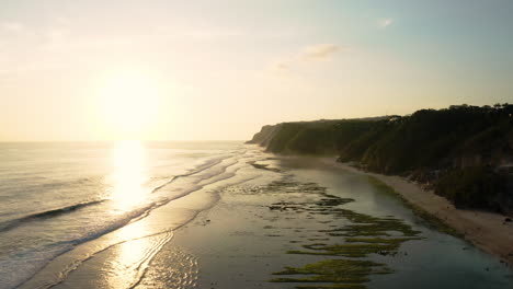 Sol-Dorado-Bajo-Que-Se-Refleja-En-Las-Aguas-Tropicales-De-La-Playa-De-Melasti,-Bali,-Cámara-Lenta-Aérea