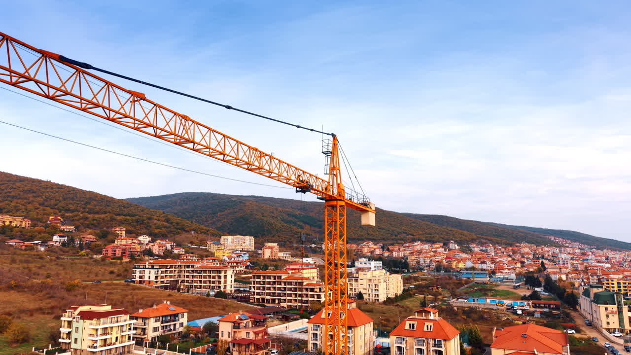 Una gru edile si erge sopra l'area residenziale. Pendii montuosi con edifici a più piani sullo sfondo.