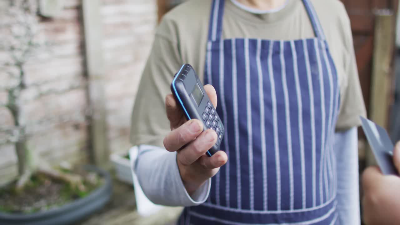 jardinero caucásico que vende plantas, usando pagos sin contacto en el centro de jardinería
