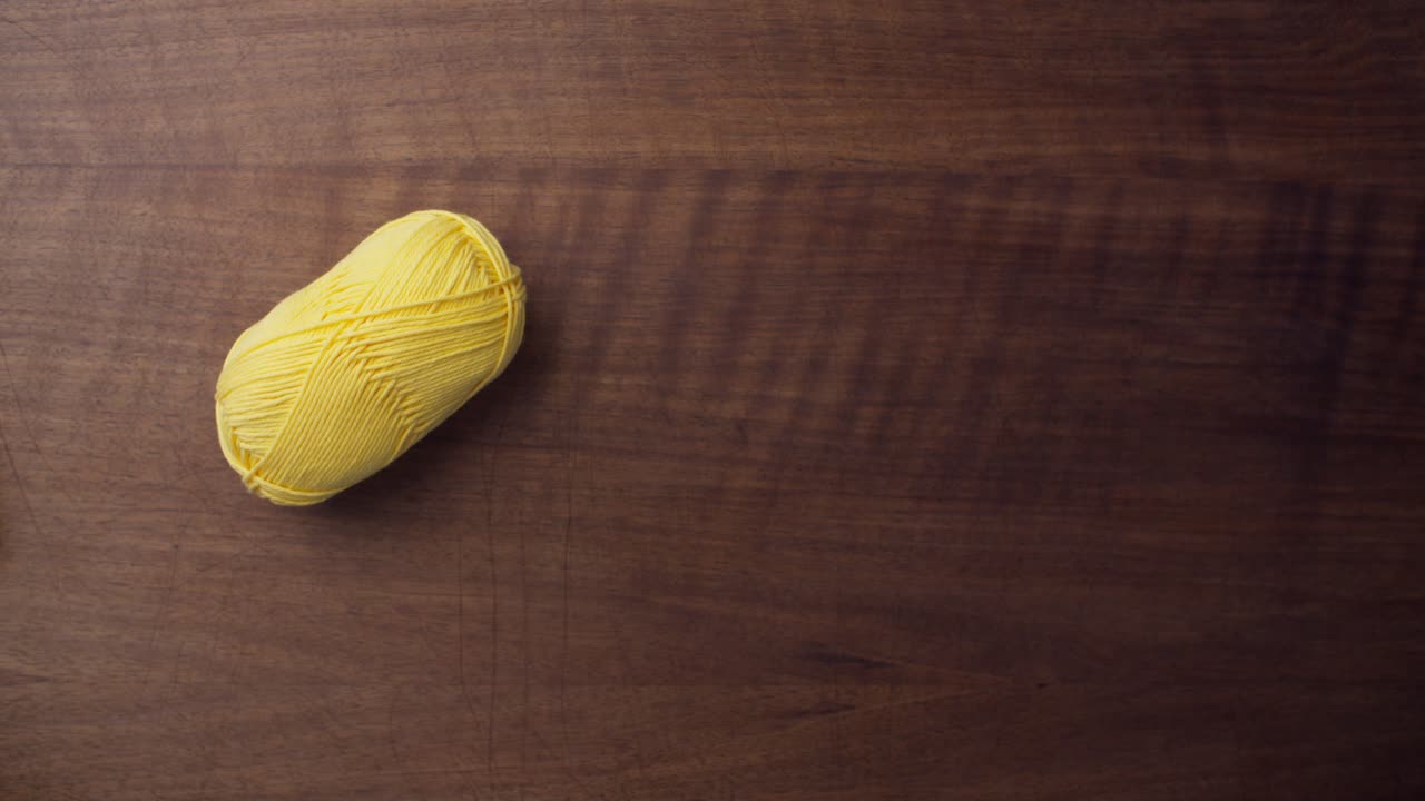 갈색 테이블 위에 노란색 크로셰 울 조각과 바늘을 올려놓은 여성의 중간 클로즈업 샷