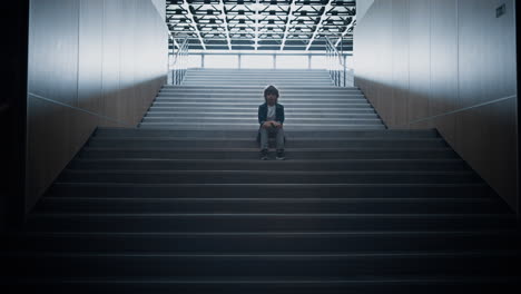 Stressed schoolboy stay alone on stairway close up. Boy hiding in school hall.